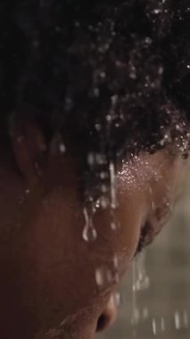 Dikey yakın plan, genç Afrikalı Amerikalı kadın evinde duş alıyor. Siyah afro kız banyoda başını ıslatıyor ve kendine bakmaktan zevk alıyor. Sabahları ev içi temizlik kavramı.