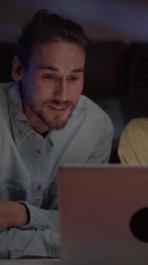 Dikey. Geceleri oturma odasında bilgisayar kullanan neşeli, çok ırklı genç bir çift. Beyaz adam ve afro kadın evde dizüstü bilgisayara bakarak sohbet ediyorlar. Mutlu insanlarda ev hayatı.