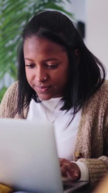 Dikey neşeli Afrikalı Amerikalı kadın dizüstü bilgisayarda sosyal uygulamaları kullanıyor evdeki kanepede rahat oturuyor. Oturma odasında sohbet eden, bilgi almak için yazı yazan oldukça siyah bir Z jenerasyonu kadın.