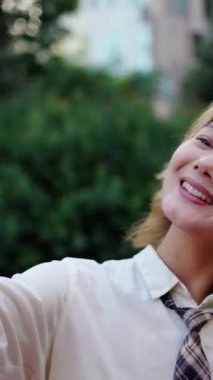 Dikey. Z jenerasyonu güzel Asyalı kadın şehir parkında selfie pembe telefon fotoğrafı için mutlu poz veriyor. Genç neşeli Çinli kadın sosyal ağ kurmak için hücreyi kullanıyor. Mobil uygulamalara bağımlı insanlar 