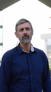 Dikey. Çekici, olgun, beyaz saçlı, beyaz iş adamı kendine güvenen ve başarılı bir ifade takınıyor. Yakışıklı profesyonel erkek, iş yerinin dışındaki kameraya doğru adım atıyor.