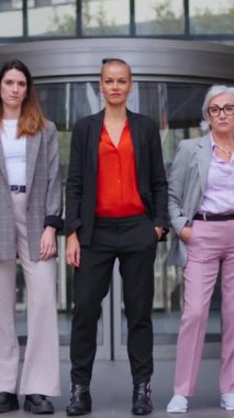 Dikey. Kamerayı traş eden kadın. Resmi takım elbiseli, elleri ceplerinde kendine güvenen bir grup iş adamı. Gururlu ve başarılı yetişkin kadın girişimciler açık havada iş arkadaşları.