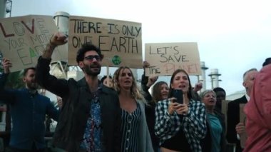 Çevre kirliliğine ve fabrikalara karşı düzenlenen gösteride çeşitli aktivistlerden oluşan bir grup, yumruklarını kaldırırken ve küresel ısınmayla ilgili mesajlar içeren pankartları tutarken öfkeyle slogan atıyorlar.