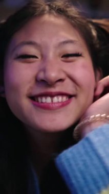 Neşeli gülümseyen Asyalı genç bir kadının dikey portresi. Çinli çapkın kadın kameraya gülüyor. Güzel, pozitif kız elini uzatıyor. Gece evde mutlu insanlar var.