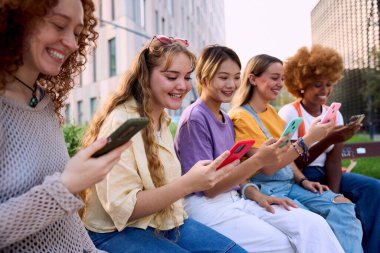 Parkta eğlenirken cep telefonu kullanan ve gülen bir grup genç kadın. Sadece kızlar akıllı telefon uygulaması hakkında dedikodu yapar. Çevrimiçi platformlarla milenyum insanlarına bağlanıyor. Sosyal medya 