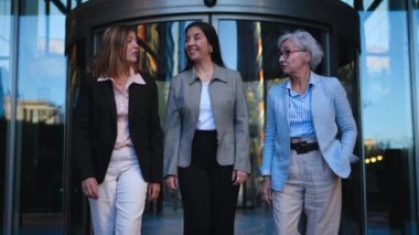Resmi olarak güçlendirilmiş üç yetişkin iş kadını kameraya doğru yürüyorlar ve modern ofis merkezinin dışında arkadaşça konuşmayı kesiyorlar. Sadece profesyonel bayan iş arkadaşları işini takım elbiseyle bırakır.