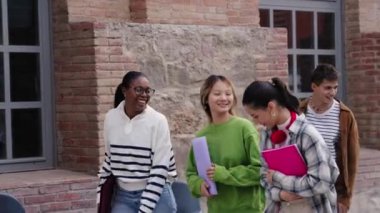 Çeşitli mutlu kız öğrenciler kampüste neşeyle dolaşıyorlar. Bir grup çok ırklı genç arkadaş birbirlerine gülüyor ve dışarıda tasasız bir şekilde dolaşıyorlar. Uluslararası üniversite insanları 