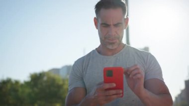 Beyaz, yakışıklı, yetişkin, güçlü, açık havada cep telefonu kullanan bir adam. Spor giyim sektöründe çekici, olgun bir erkek sporcu. Lensli kırmızı arabaya bakıyor.