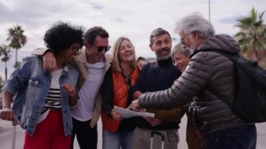 Çok ırklı yetişkin insanlar bir araya gelip turistik yerleri tartışıyor ve tatil şehrindeki seyahat kâğıdı haritasına neşeli bir şekilde bakıyorlar. Olgun turizm arkadaşları açık havada buluşuyor