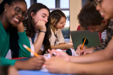 Çeşitli Gen Z üniversite öğrencileri bir araya gelip kampüs çalışmasında ödev yapıyorlar. Müfredattan geçen çok ırklı genç liseli insanlar fakülte masasında otururken gülümseyerek notlar alıyorlar.