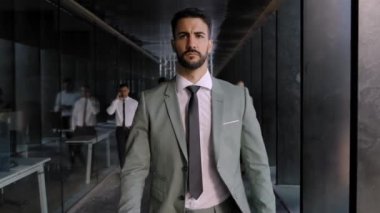 Kendine güveni olan yakışıklı yetişkin bir adam ofis koridoruna doğru yürürken çeşitli meslektaşları kalabalıklaştı. Çekici, başarılı, takım elbiseli bir yönetici ciddi bir ifadeye bakıyor.
