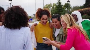 Kafkasyalı kadın konuşuyor ve şehirdeki neşeli genç kadın grupları tarafından cep telefonuyla daire içine alınıyor. Sarışın kız grup arkadaşlarına cep telefonu ekranını gösteriyor. Dışarıda birlikte duruyorlar.