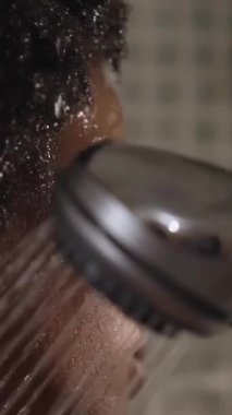 Dikey olarak genç siyah afro kadın evinde duş alıyor. Afro-Amerikalı kadın gözleri kapalı, yüzünü ıslatıyor ve saçlarını yaptırıyor. Daire banyosunda kendine bakmaktan zevk alıyor. Günlük kişisel temizlik.