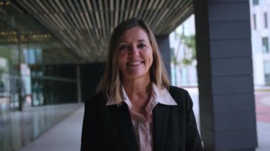 Açık havada mutlu ve gururlu bir ifadeyle kameraya gülümseyen olgun sarışın iş kadını. Kafkasyalı profesyonel kadın ofis binasının atari salonlarında neşeli pozlar veriyor. 