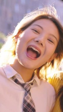 Dikey. Sadece komik jestler yapan bir grup Asyalı genç kadın dışarıda kameraya yakından bakıyor. Üç güzel kuşak z Çinli bayan arkadaş gülüyor güneşli bir günde kucaklaşıyorlar.