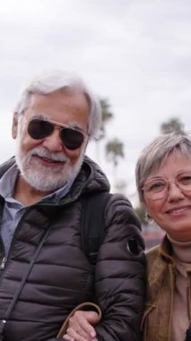 Dikey. Kafkasyalı romantik turist çifti birbirine aşık bir şekilde poz veriyor. Tatilin tadını çıkarıyor. Şehre sarılıyorlar. Yaşlı gri karı koca emeklilik turizminde kameraya gülümsüyor.