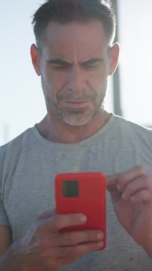 Dikey. Beyaz, yakışıklı, yetişkin, güçlü, açık havada cep telefonu kullanan bir adam. Spor giyim sektöründe çekici, olgun bir erkek sporcu. Lensli kırmızı arabaya bakıyor.