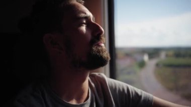 Sakallı genç beyaz adam trenin camından dışarı bakıyor. Gezgin erkek demiryolunda düşünceli ve rahat bir şekilde seyahat ediyor. Göçebe İnsanlar toplu taşıma araçlarıyla seyahat eder. Arka planda peyzaj alanı gün batımı