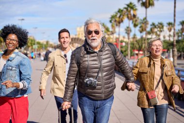 Bir grup olgun turist, yolculuk yerlerine geç kaldıkları için valizleriyle şehir caddesine doğru koşuyorlar. Endişeli turizm arkadaşları tatilde aceleyle seyahat ediyorlar.