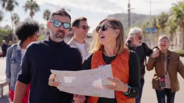 Bir grup bavulu olan turist arkadaşlarıyla orta yaşlı bir çift yürüyor, bakıyor ve bir seyahat haritası tutuyor. Avrupa kenti sokaklarında tatil yapan insanların turizmi