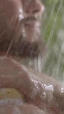 Dikey. Genç, uzun saçlı adam banyoda sabun temizliyor. Yetişkin, beyaz, sakallı bir erkeğin duşta günlük kişisel bakım ve hijyen işlerini tek başına yapması.