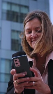 Dikey. Alçak açılı, olgun, sarışın, resmi iş kadını. Demiryoluna yaslanmış, dışarıda mutlu bir ifadeyle cep telefonuna bakıyor. Ofiste çalışırken cep telefonu kullanan profesyonel beyaz kadın. 