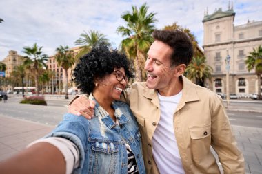 Mutlu çok ırklı yetişkin turist çifti. Birbirlerine bakarak selfie çekiyorlar. Açık havada sarılmışlar. Orta yaşlı aşık insanlar turizmi gülümsetiyor. Şehir sokaklarında tatilin tadını çıkarıyorlar. 