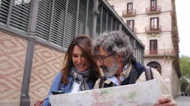 Bir çift Kafkasyalı yetişkin insan ellerinde haritayla turizm şehrinin caddesinde bir yeri arayarak konsantre bir şekilde yürüyorlar. Yaşlı turistler tatilleri ya da birlikte kaçamakları severler.