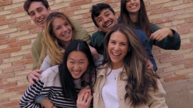 Neşeli bir grup genç arkadaş arka planda tuğla duvarla eğleniyorlar. Çok ırklı Z nesli, insanları heyecanlandırdı. Dışarıdaki insanların kameralara gülüp kucaklaşmasını izlediler.