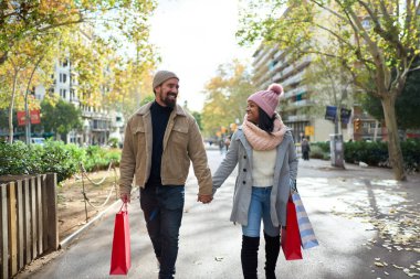 Güzel, genç ve ırklar arası bir çift şehrin sokaklarında kış tatilinin tadını çıkarıyor, yürüyüş yapıyor, bir yeri işaret ediyor, dışarıda Noel 'i kutlarken kucaklaşıyor ve hediye çantalarını tutuyor.