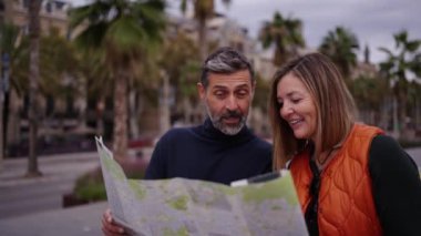 Olgun Kafkasyalı turist çifti elinde kağıt haritayla, sonbahar tatilinin tadını çıkaracağı yerleri gösteriyor. Orta yaşlı bir çift gülerek Avrupa şehir merkezini geziyor. Yetişkinlerin orta yolu 