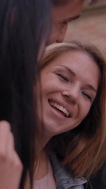 Dikey. Neşe dolu bir grup arkadaş, şehir caddesinde birlikte durup kucaklaşırken eğleniyor. Mutlu üniversiteli genç insanlar dışarıda gülüp kucaklaşarak toplandı. Öğrenci topluluğu kavramı