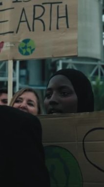 Dikey. Ciddi bir Afrikalı kadın eylemci dışarıda barışçıl bir gösteride pankart tutuyor. İklim değişikliği ve küresel ısınma kirliliği konusunda çeşitli cesur insanlar gruplar halinde