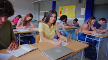 Ergen kız öğrenci, sınıfta sınıf arkadaşlarıyla masada oturmuş kameraya gülümseyen pozlar veriyor. Grup halinde çalışan liseli insanlar sınıfa yoğunlaşmışlar. Sınava giren mutlu beyaz kadın. 