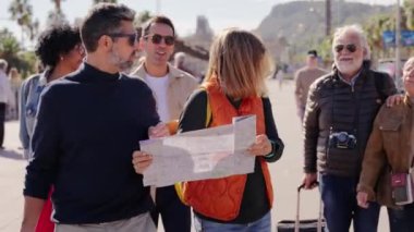 Yetişkin, beyaz bir çift ellerinde kağıt haritayla turistik yerleri ve bavulları olan turistik yerleri geziyorlar. Turizm insanları güneşli şehir sokaklarında tatilin tadını çıkarıyorlar.