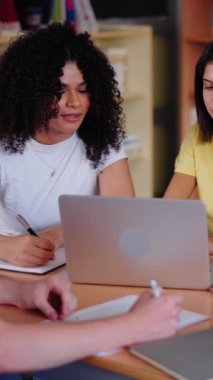 Dikey. Lise öğrencilerinden oluşan çeşitli gruplar kütüphanede dizüstü bilgisayarlar kullanarak birlikte çalışırken genç adam not defterlerine not alıyor. Mutlu Gen Z sınıf arkadaşları sınıf projesi için çalışıyor.