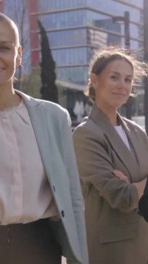 Dikey. İş merkezinin dışında kendine güvenen farklı kadın profesyonellerin takım portresi. Gülümseyen bir grup resmi çalışan kadın dışarıda kameraya bakıyor. Zarif iş arkadaşlarının videosu