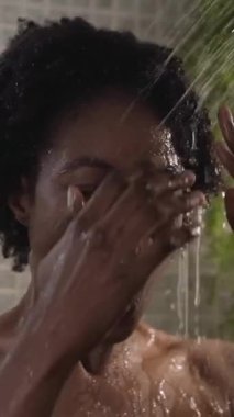 Dikey. Genç afro kadın evde tek başına duş alırken neşeli bir şekilde şarkı söyleyip dans ediyor. Afro-Amerikan mutlu kadın pozitif enerjili saçlarını ıslatıyor. Kişisel bakım ve vücut hijyeninin tadını çıkarıyor.