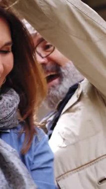 Dikey. Yetişkin çiftler gülerek ve dışarıda sonbahar günü el ele tutuşarak dans ederken eğleniyorlar. Beyaz saçlı adam ve beyaz kadın şehir caddesinde birlikte mutlular. Neşe, aile ve aşk