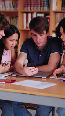 Dikey. Çeşitli lise öğrencileri kütüphanede cep telefonuna şaşırmış görünüyor. Neşeli Gen Z sınıf arkadaşları çok ırklı arkadaşları hücrede oturuyor ve derslerine ara veriyorlar.