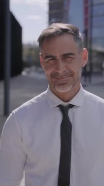 Dikey. Kameraya gülümseyen olgun bir adamın portresi iş binasının önünde mutlu bir şekilde duruyor. Profesyonel yönetici kendine güvenen çapraz kollar yapıyor. Gri saçlı, resmi yakışıklı, erkek.