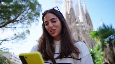 Barcelona 'da Sagrada Familia' nın önünde cep telefonu kullanan genç bir bayan arkadaş. Avrupa 'daki güzel beyaz kızlar tatilin tadını çıkarıyorlar ve gülümsüyorlar. Komik turizm insanları gülümser.