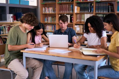Farklı lise öğrencileri kütüphanedeki not defterlerine not alarak birlikte çalışırken beyaz bir adam dizüstü bilgisayara yoğunlaşarak oturuyor. Gen Z sınıf arkadaşları sınıf projesi için çalışıyor