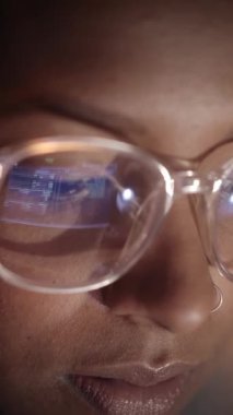 Dikey. Karanlıkta dizüstü bilgisayarla çalışan bir kadının gözlüklerindeki bilgisayar ekranının yansımasına yakın çekim. Bilgisayar ağı güvenliği ve internet kavramı. Yüksek kalite 4k görüntü