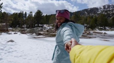 POV Mutlu turist el ele tutuşuyor ve güzel donmuş dağ gölünü aşıyor, birlikte kış tatilinin tadını çıkarıyor.