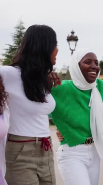 Dikey. Neşe dolu çeşitli gruplar. Sadece bayan arkadaşlar dışarıda sırayla yürür. Eğlenceli, hoş, genç bir bayan topluluğu. Birlikte gülüp eğleniyorlar. Şehir parkında geziniyorlar.