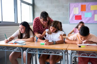 Bir öğretmen sınıftaki bir öğrenciye bireysel rehberlik eder, katılımını teşvik eder ve öğretici ve destekleyici bir öğrenme ortamında anlayış gösterir.