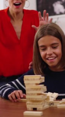 Dikey. Mutlu nesil aile evde Jenga oynamak için toplandı. Beyaz insanlar birlikte ev yaşamının masa oyunlarını oynuyorlar. Odaklanmış gülen bir kız kuleden ahşap bloğu alıyor.