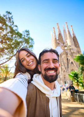 Dikey. Barcelona 'da Sagrada Familia' nın önünde selfie çeken genç bir çift. Şehrin sokaklarında gülümseyen karı koca tatilin tadını çıkarıyor ve gülümsüyor. Komik turizm insanları.