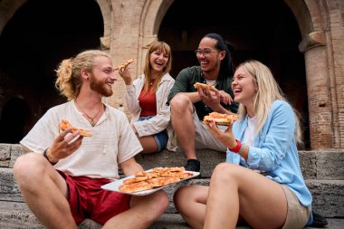 Komik bir grup genç ve turistik şehirde pizza yerken eğleniyorlar. İtalyan arkadaşlar dışarıda yemek yiyor, sokak ortamında gülüyorlar. Canlı şehir geçmişi ve neşeli bir ruh hali.